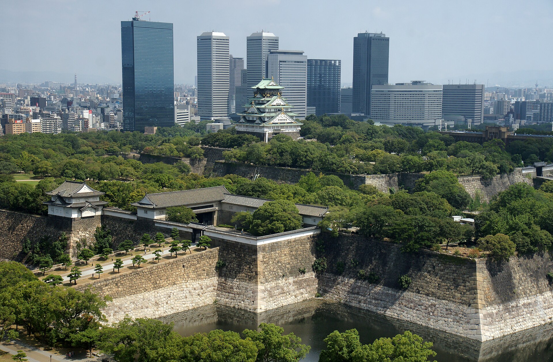 從高處俯瞰大阪城 — 天守閣、大手門與千貫櫓、巨大的內堀石垣，背後是大阪商業公園的高樓群