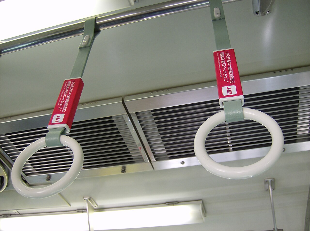 日本電車車內兩個吊環的紅色握把上印著「この付近では携帯電話の電源をお切りください。（本區域請關閉行動電話電源）」的日英雙語告示，並附有手機圖示