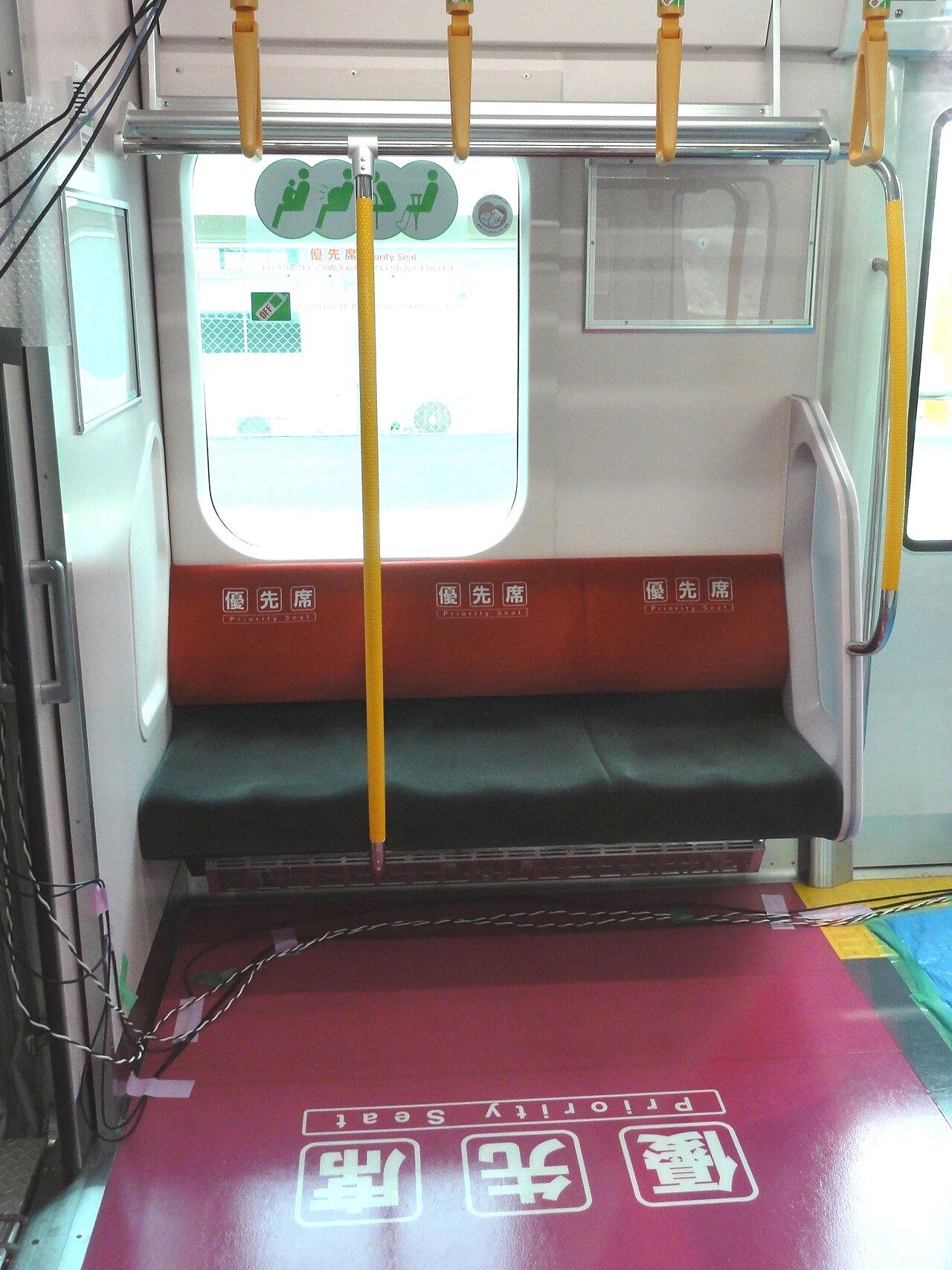 JR 東日本 E235 系電車的優先席區域 —— 座椅椅背是橘紅色並印有「優先席 Priority Seat」字樣，上方貼有孕婦、長者、身障者、傷者的綠色圖示標語，地板則鋪成深紅色並大字寫著「優先席 Priority Seat」