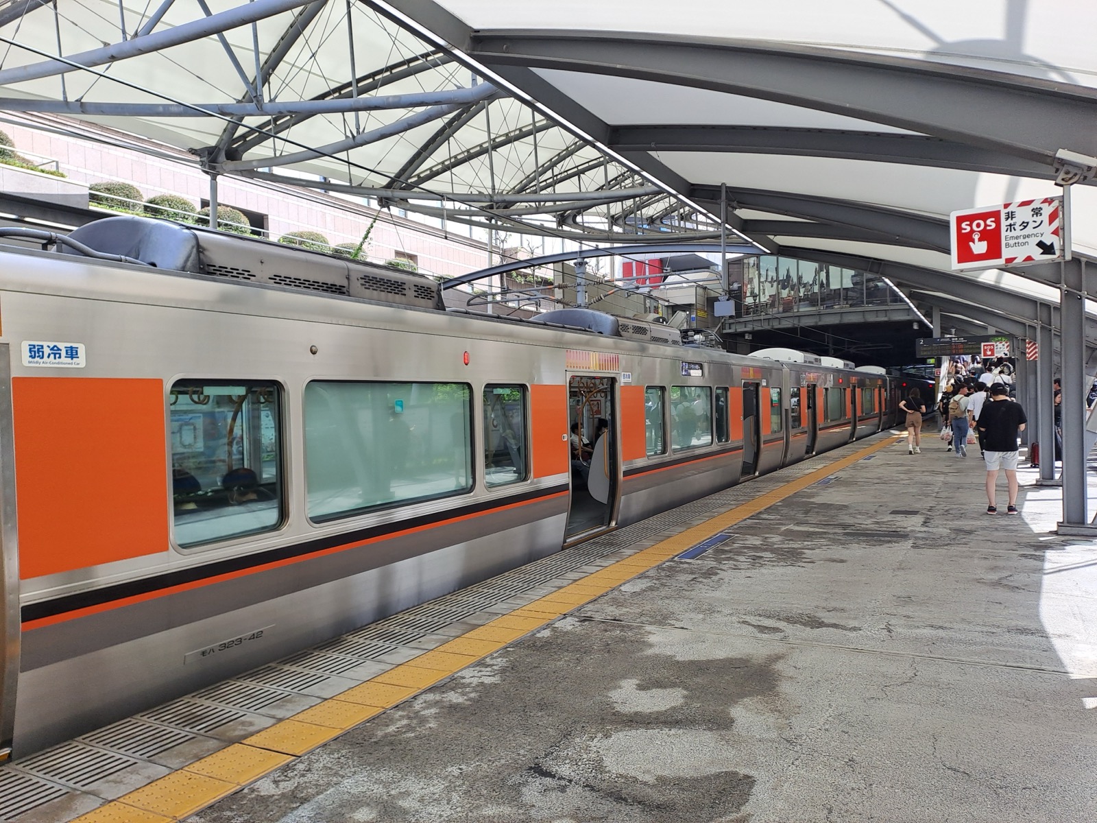 JR 西日本 323 系電車停靠ユニバーサルシティ駅月台——銀色車身配橘色飾帶的通勤電車，月台上有帳篷狀屋頂與旅客