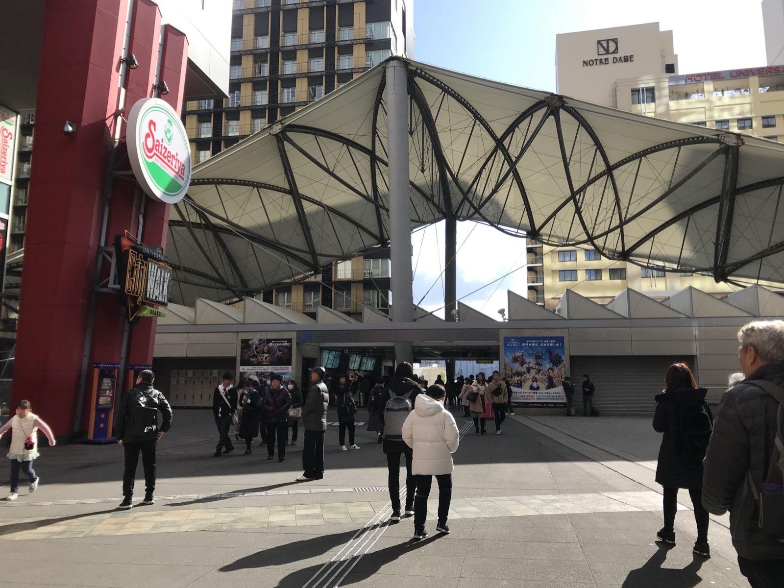 ユニバーサルシティ駅前廣場——白色帳篷狀鋼構屋頂、開闊的步道與周邊街景，旅客往來前往大阪環球影城 USJ